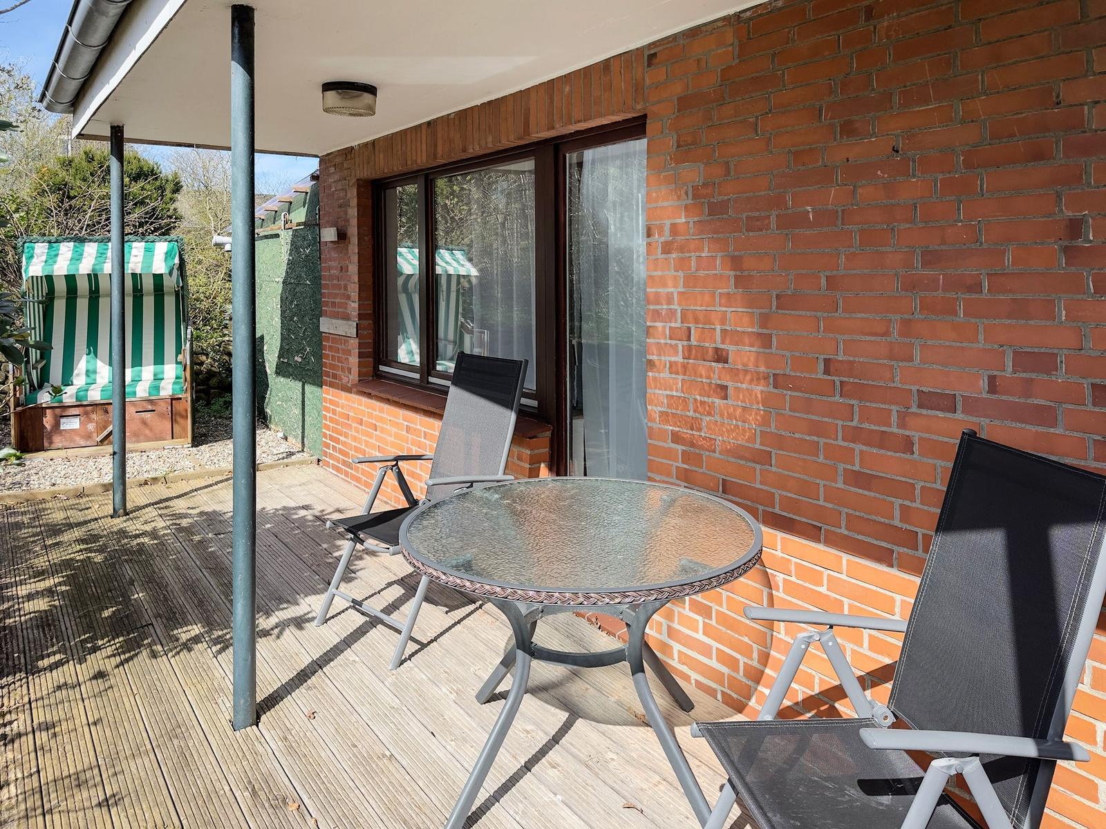 Terrace with table and two chairs, red brick wall, green beach chair in background.