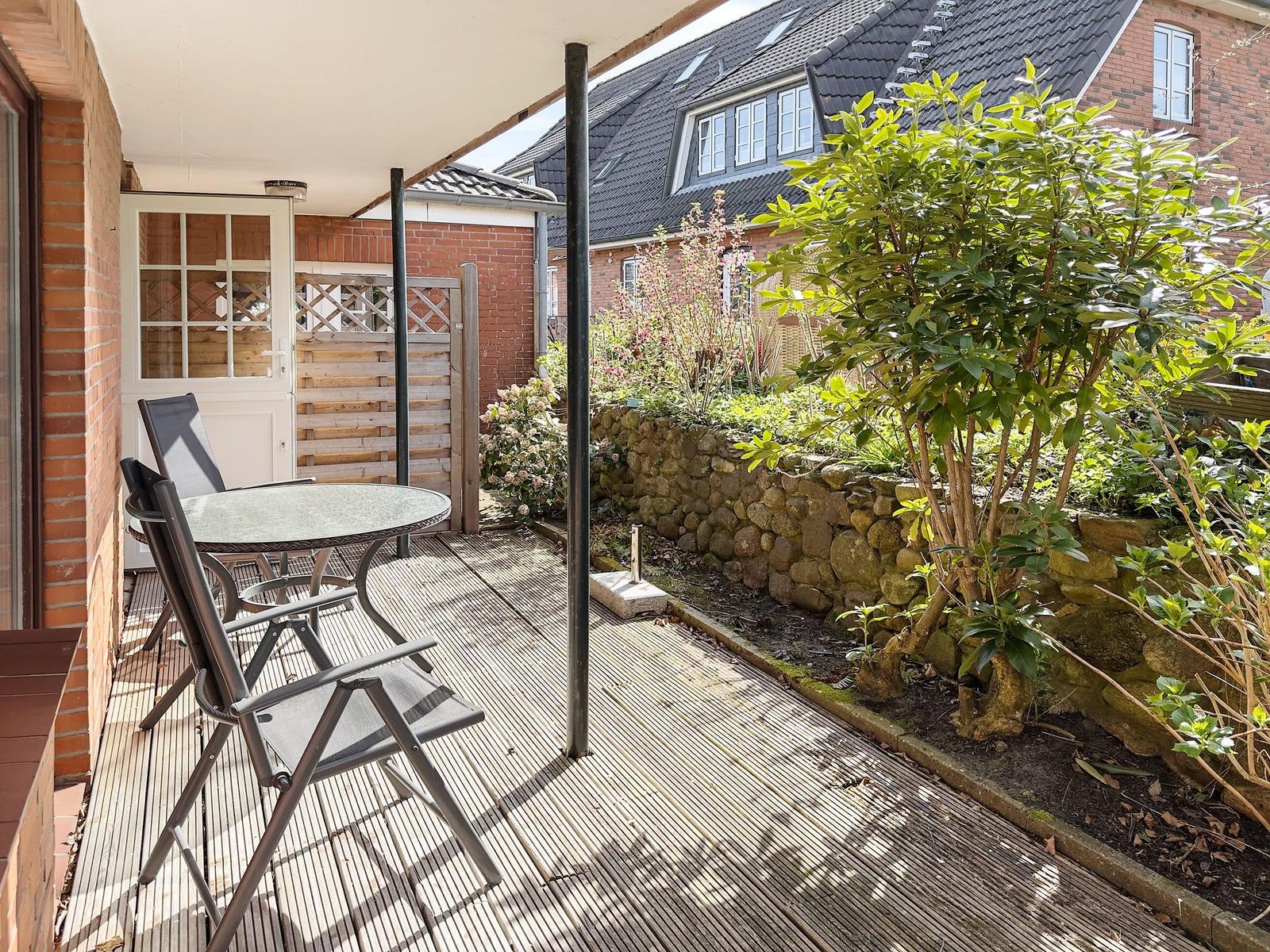 Terrace with table and chairs, surrounded by garden and stone wall.