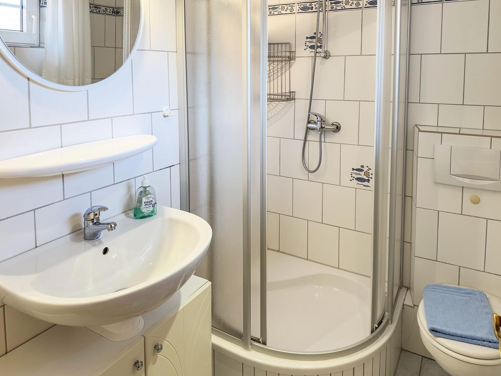 Bathroom with shower, sink, and toilet. White tiles and mirror.
