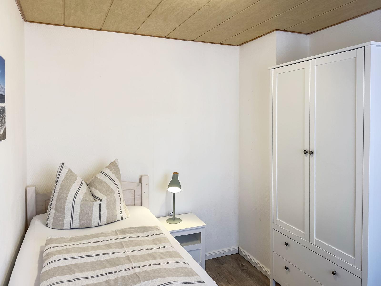 Bedroom with bed, nightstand, and wardrobe. Ceiling with wooden panels.