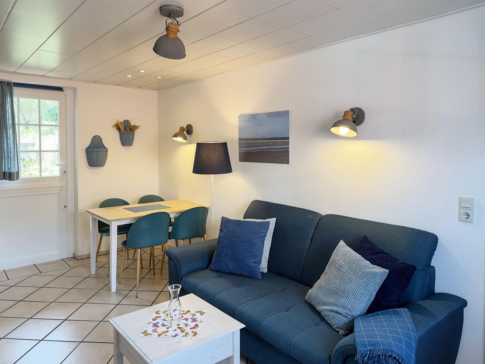 A living and dining area with a sofa, table, chairs, and wall lighting.