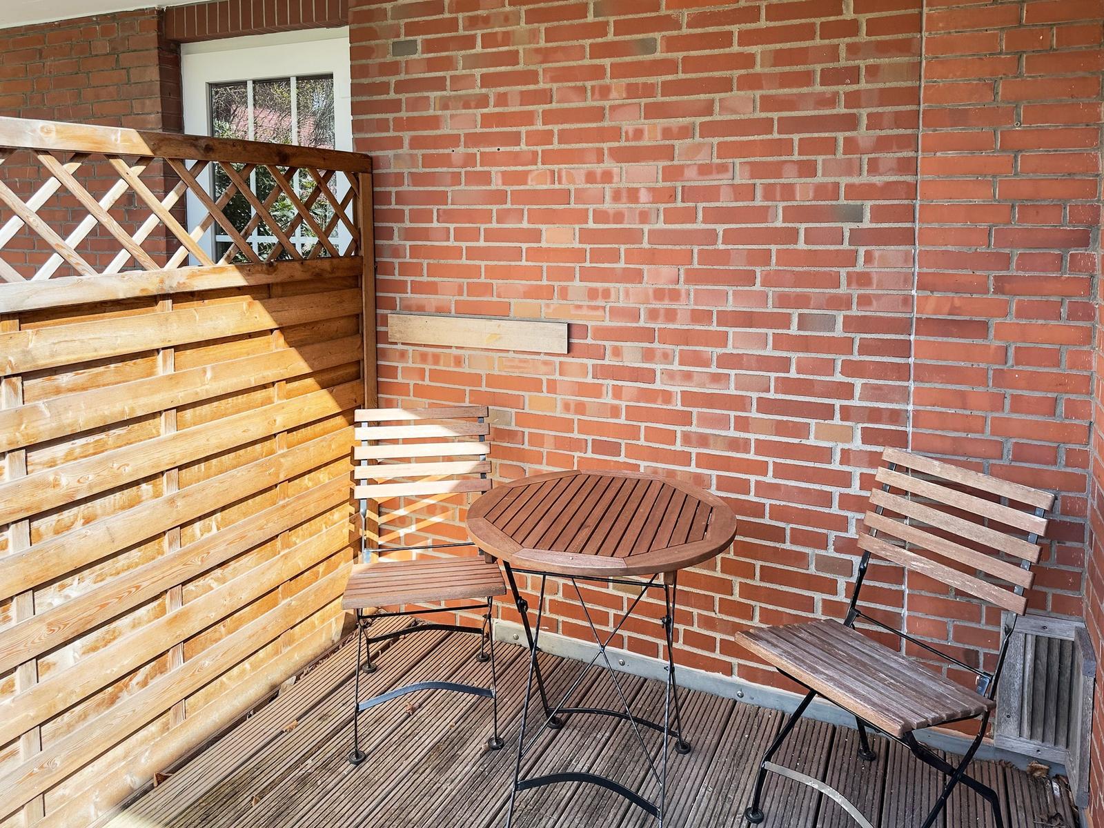 Terrasse mit Holztisch und zwei Stühlen vor roter Ziegelwand