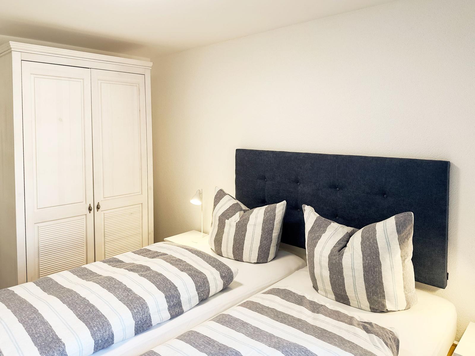 Schlafzimmer mit zwei Betten, dunklem Kopfteil und weißem Schrank.