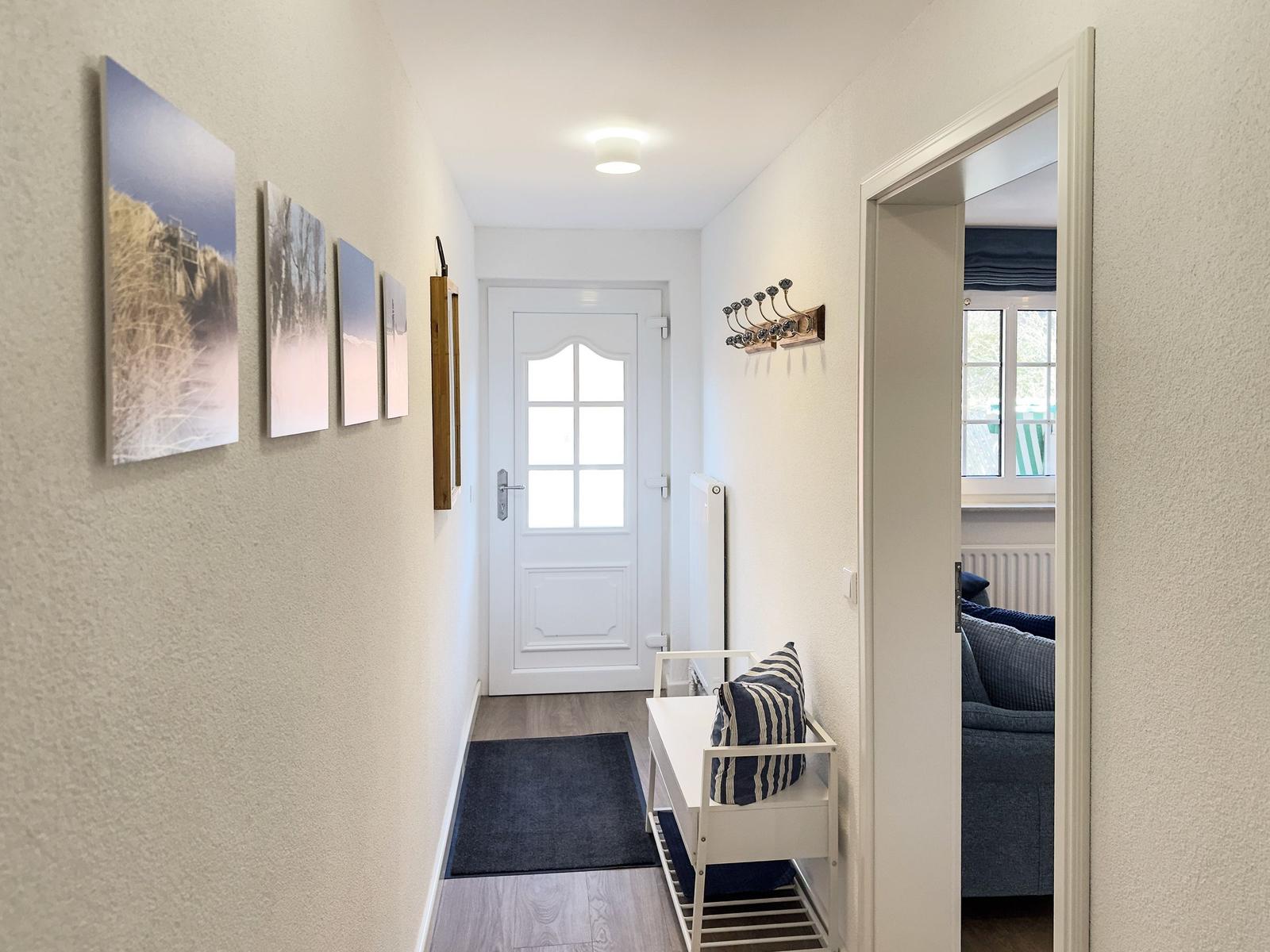 Flur mit Wandbildern, weiße Tür und Sitzbank mit Kissen.