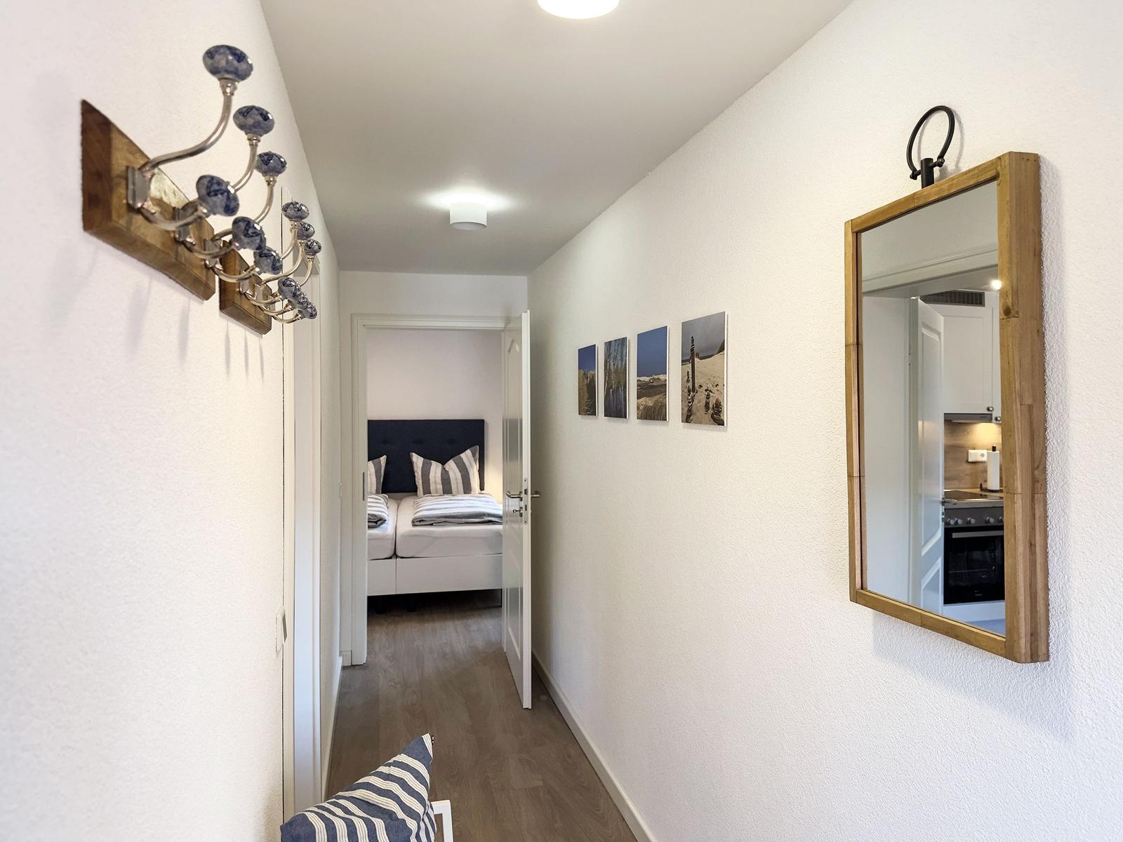 Flur mit Spiegel, Wandbildern und Blick in Schlafzimmer und Küche.