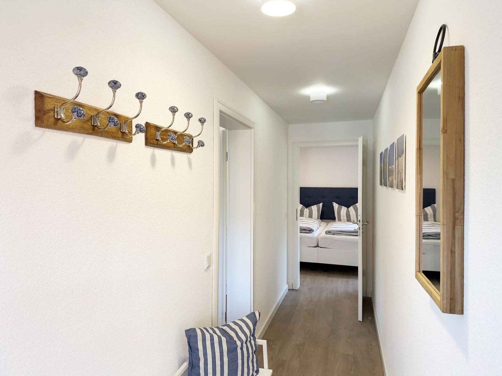 Flur mit Garderobe, Spiegel und Blick in Schlafzimmer mit Bett und Kissen.