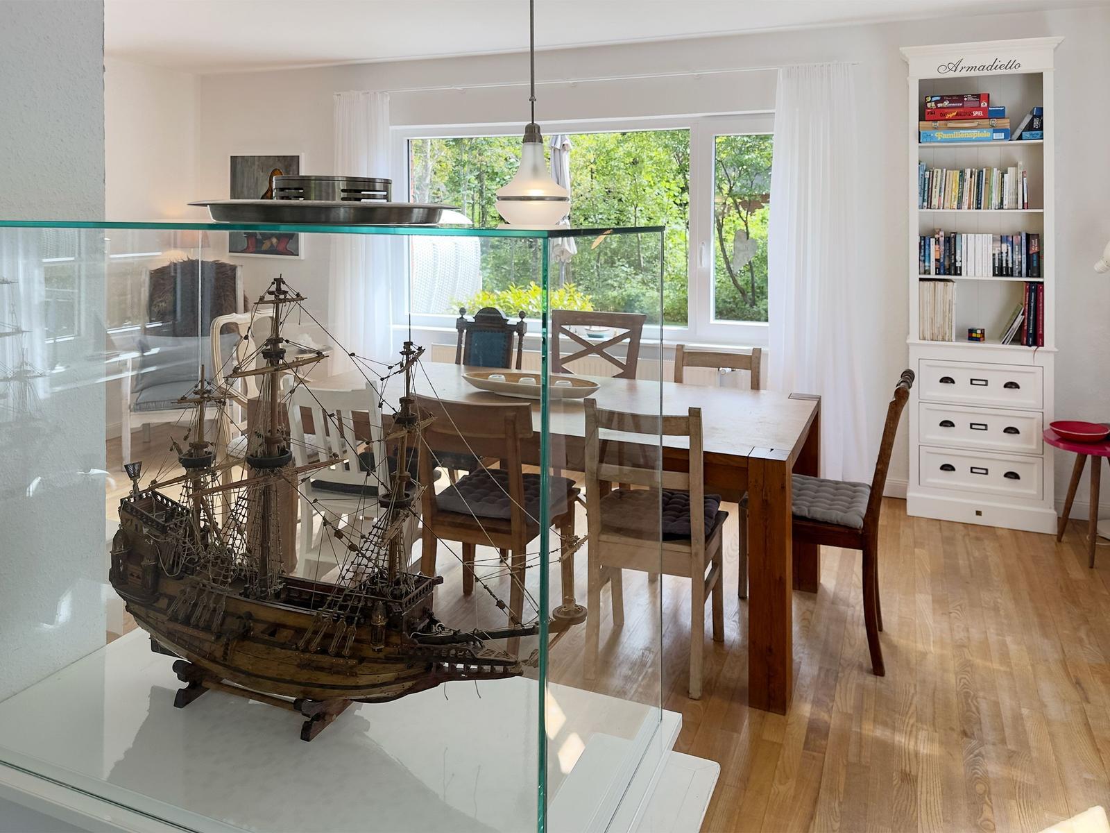 Ein Esszimmer mit Holztisch, Stühlen und einem Modellboot in einer Glasvitrine.