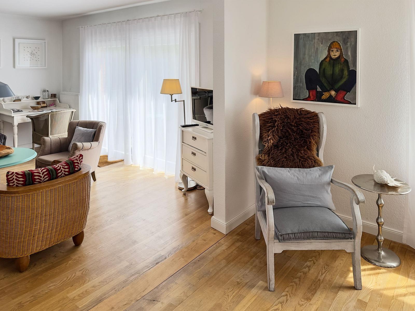 Wohnzimmer mit Holzboden, Sessel, Schreibtisch und Wandbild.