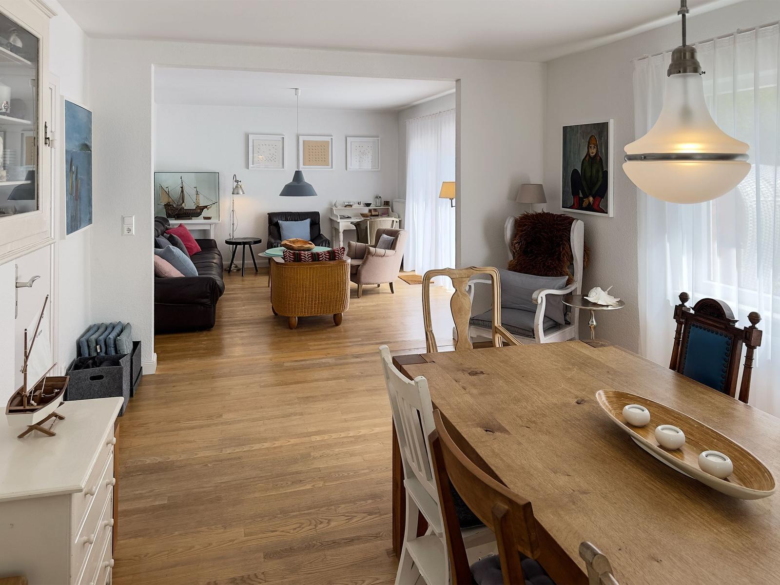Esszimmer mit Holztisch und Stühlen, Wohnbereich mit Sofa und Sessel, Holzboden und Wandbilder.