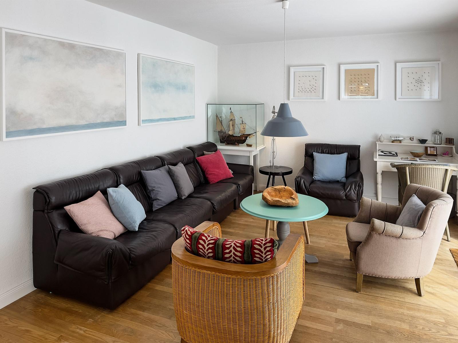 Wohnzimmer mit Sofa, Sesseln und Tisch. Wandbilder und Möbel sind sichtbar.