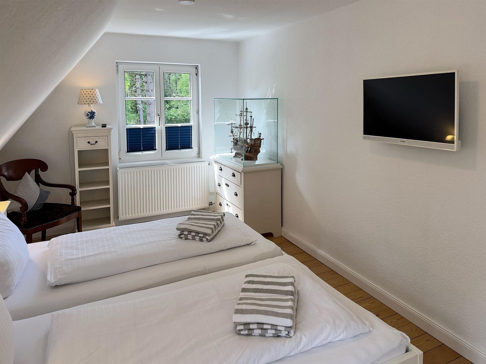 Zwei Betten, TV, Fenster mit Blick auf Wald, Schreibtisch und Stuhl.