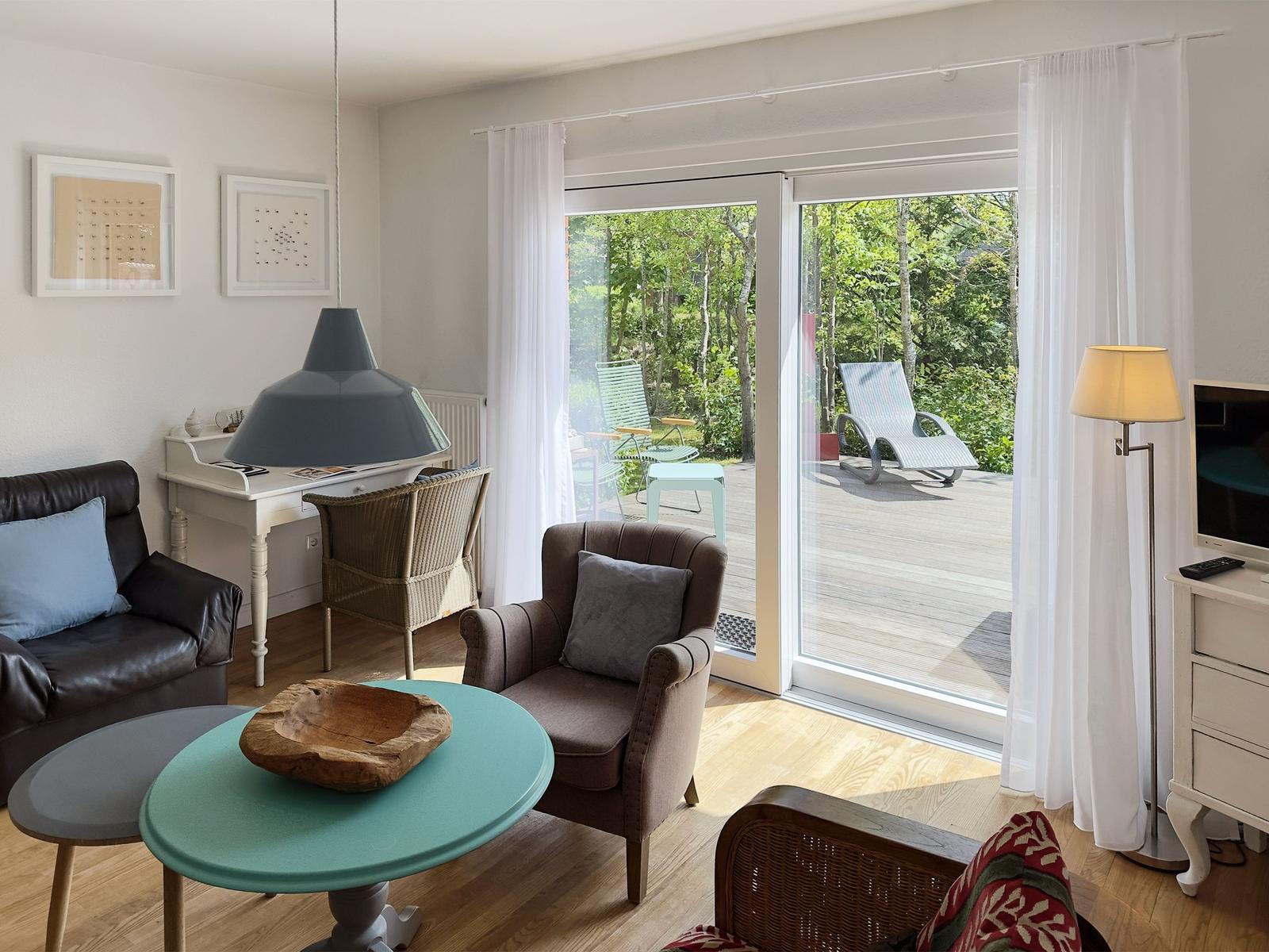 Wohnzimmer mit Sitzgelegenheiten und Blick auf die Terrasse mit Garten.