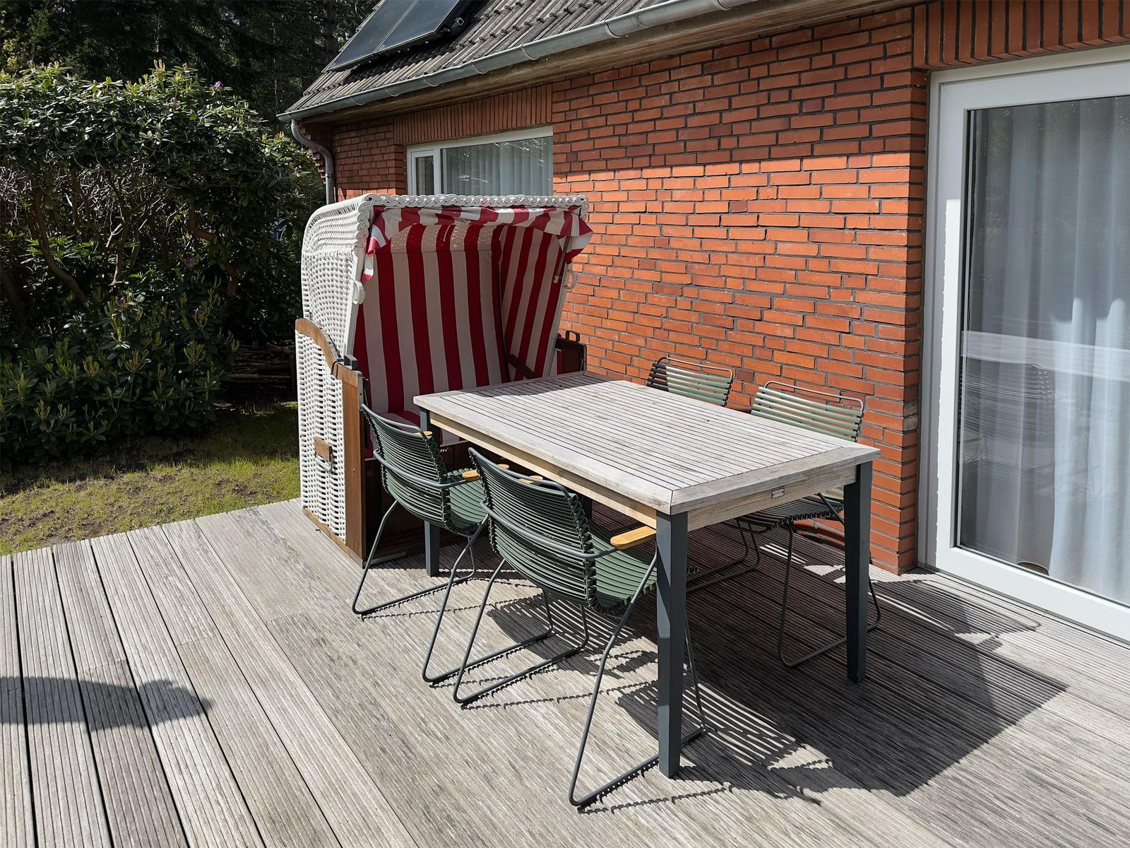 Terrasse mit Tisch, Stühlen und Strandkorb neben Hauswand.