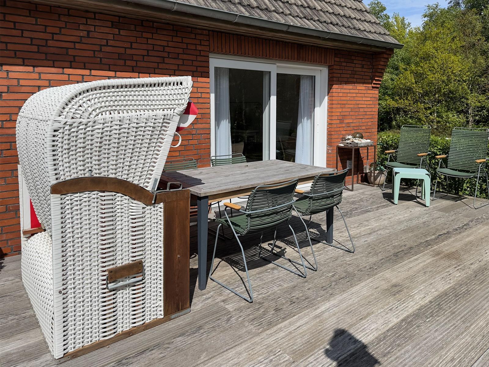 Terrasse mit Tisch, Stühlen und Strandkorb vor rotem Backsteinhaus.