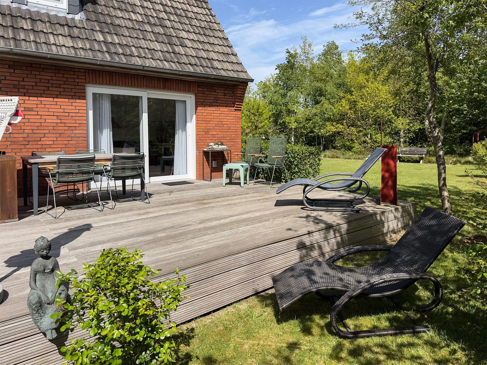 Terrasse mit Gartenmöbeln, Sonnenliegen und Blick auf Wald.