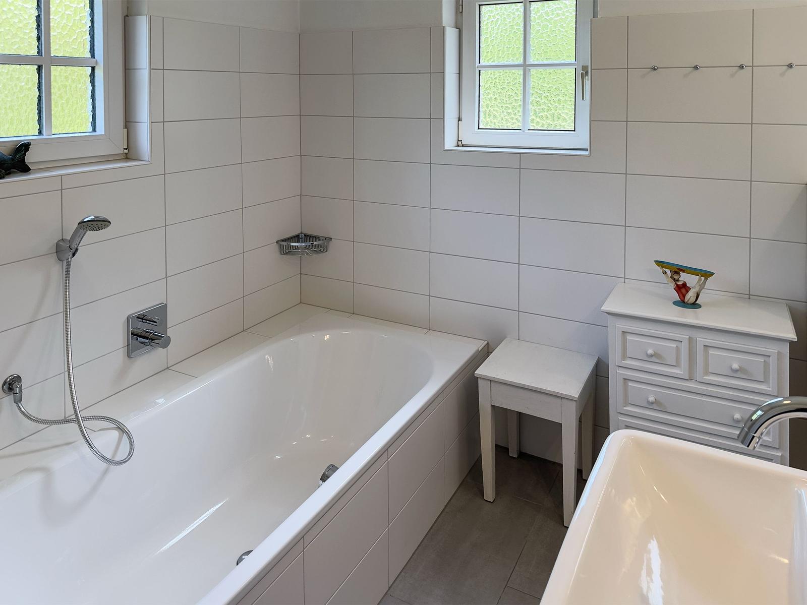Badezimmer mit Badewanne, Waschbecken und Fenstern.