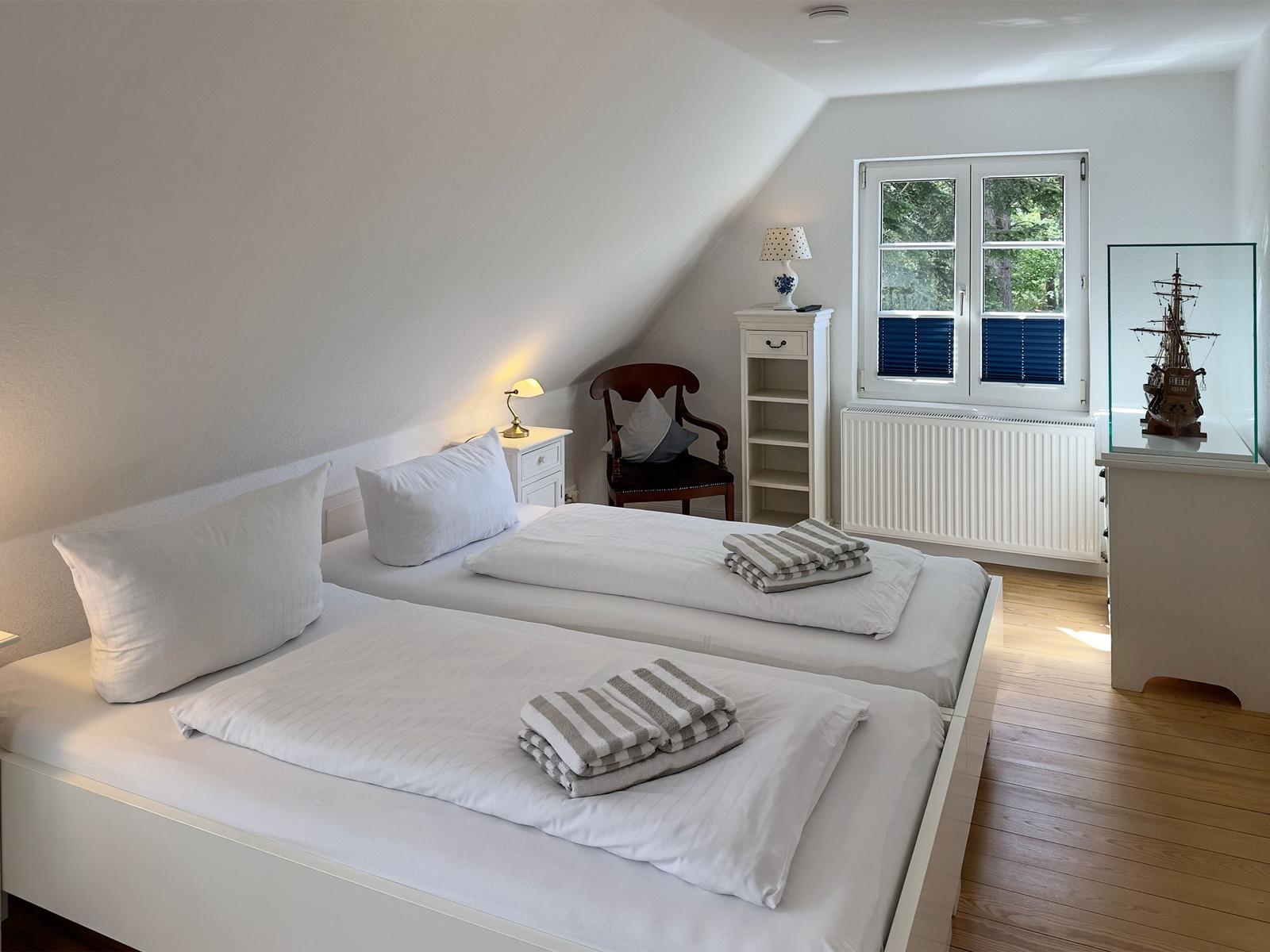 Zwei Betten mit weißen Bettwäsche, Holzboden, Fenster mit Jalousien und Schiffmodell.