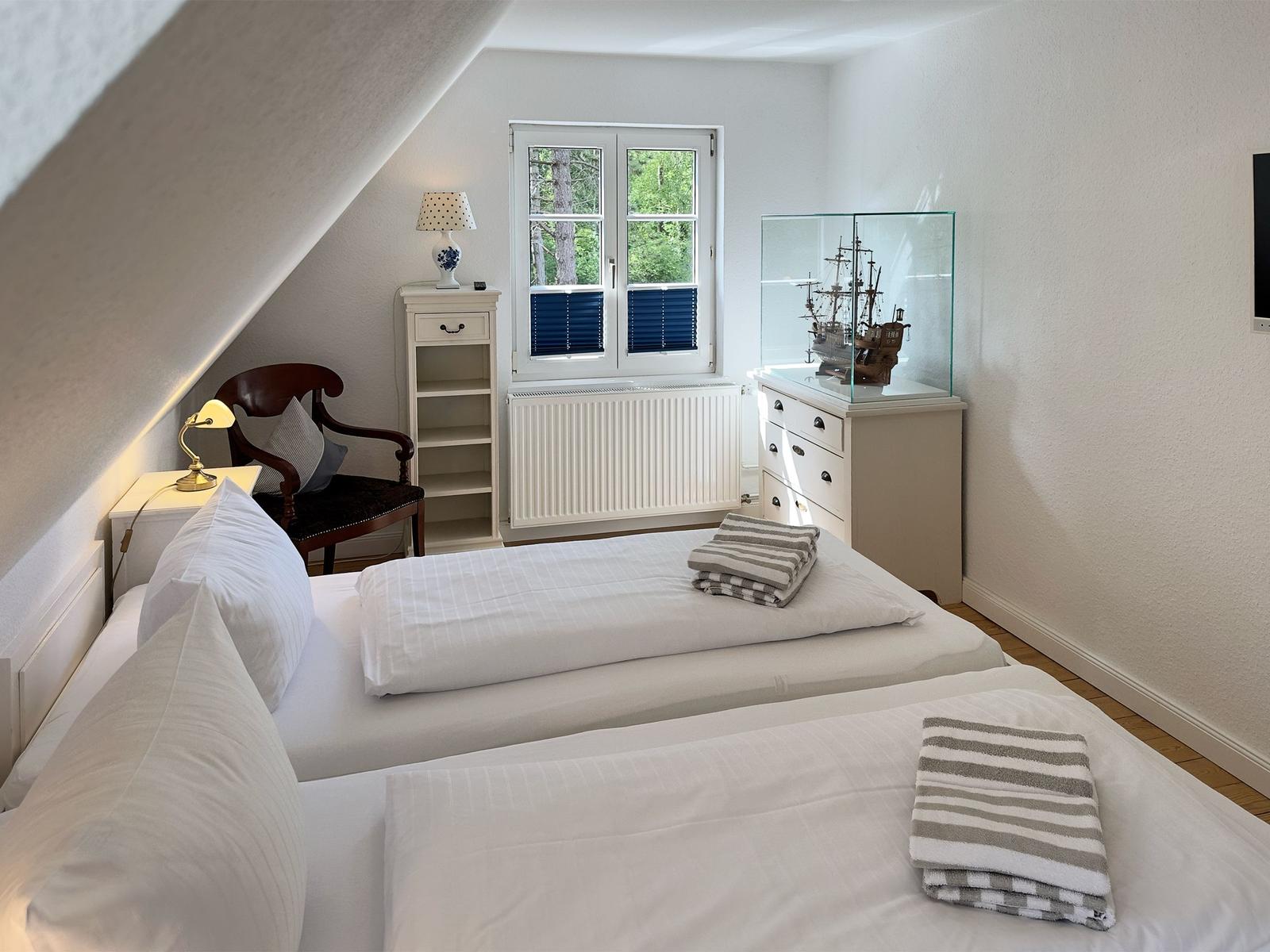 Zimmer mit zwei Betten, Fenster, Schrank und Modellboot.