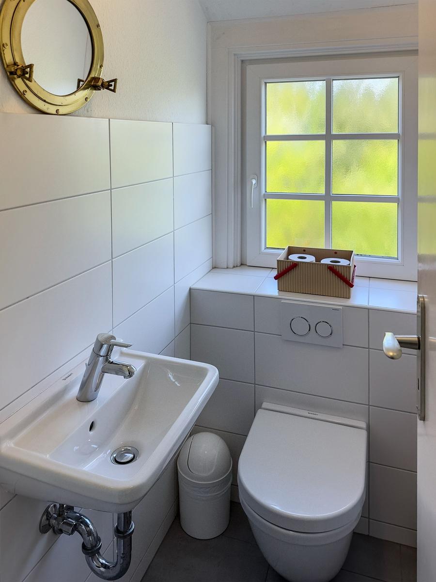 Badezimmer mit Toilette, Waschbecken und Fenster. An der Wand hängt ein runder Spiegel.
