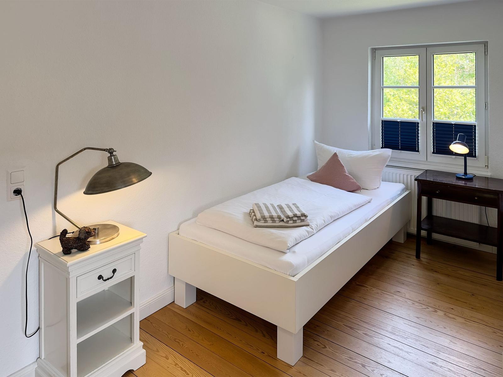 Ein Schlafzimmer mit weißem Bett, Holzboden und Fenster mit Blick auf Grün.