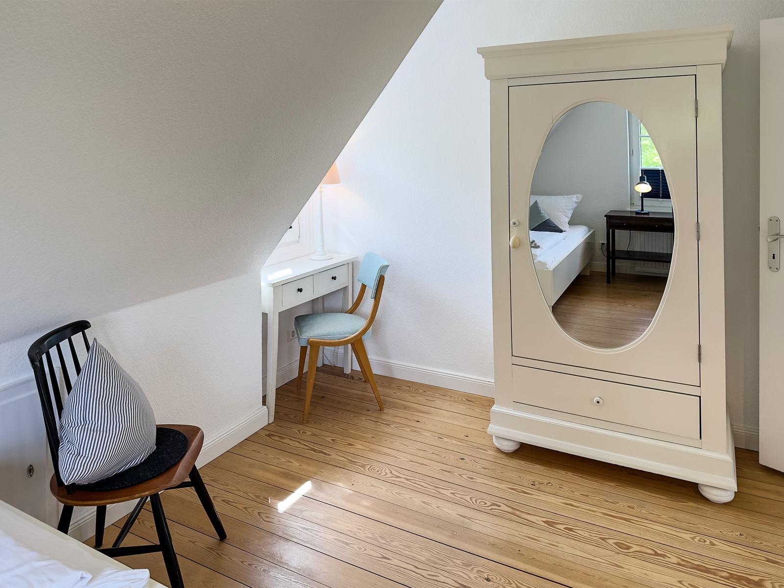 Schlafzimmer mit Kleiderschrank, Schreibtisch und Stuhl unter Dachschrägen.