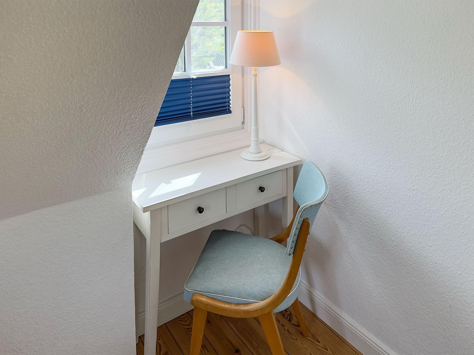 Schreibtisch mit Stuhl unter Fenster mit blauen Jalousien.