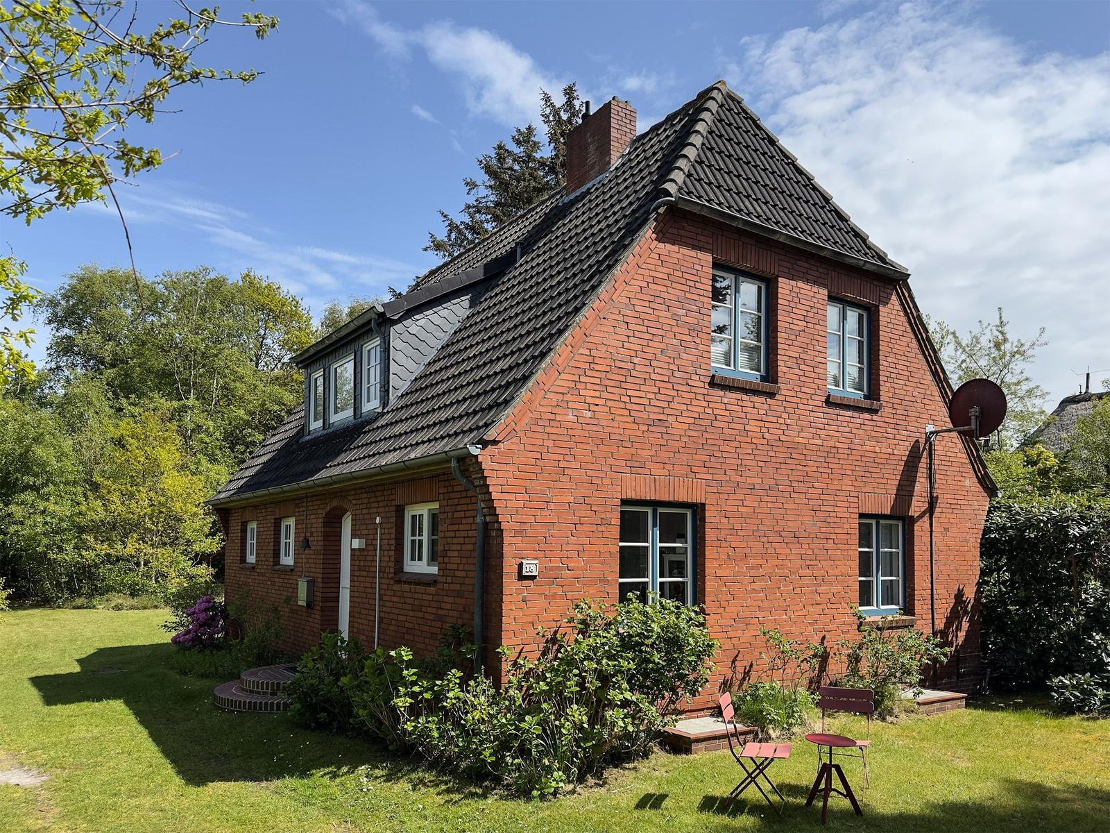 Rotes Backsteinhaus mit Garten und Terrasse unter blauem Himmel.