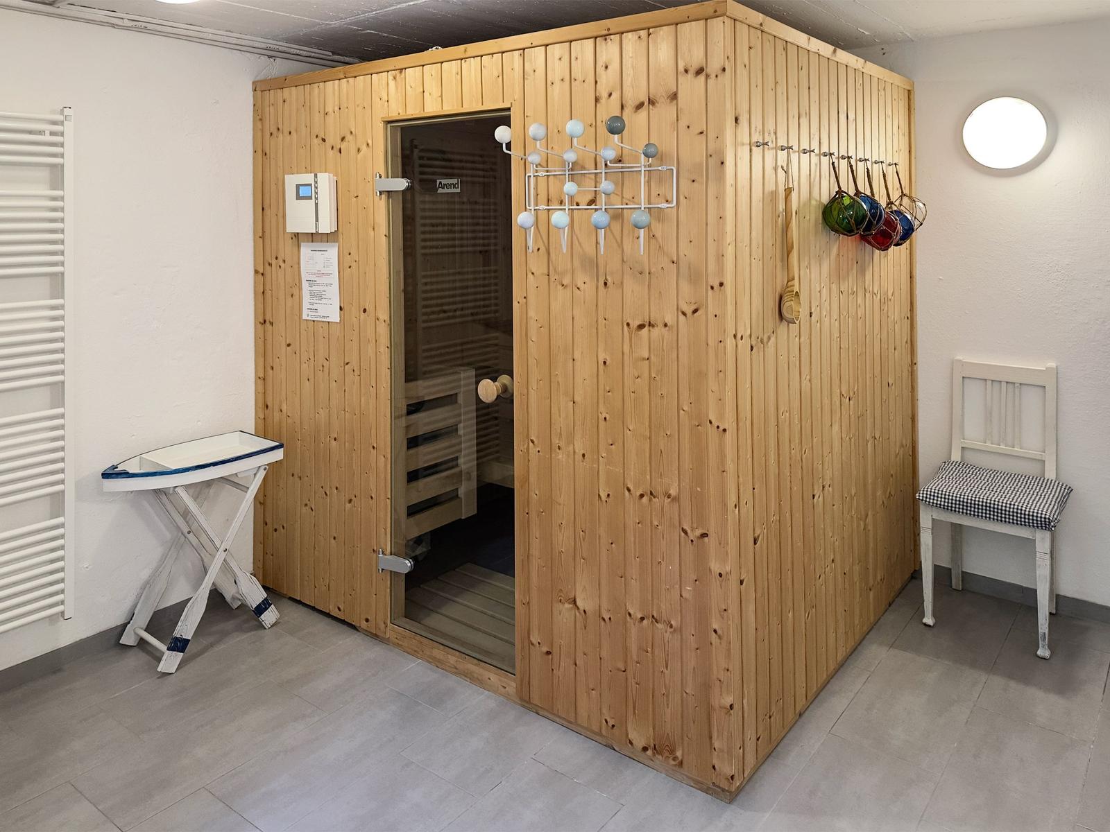 Holzsauna mit Glasfront, Stuhl und Hängeschale an der Wand.