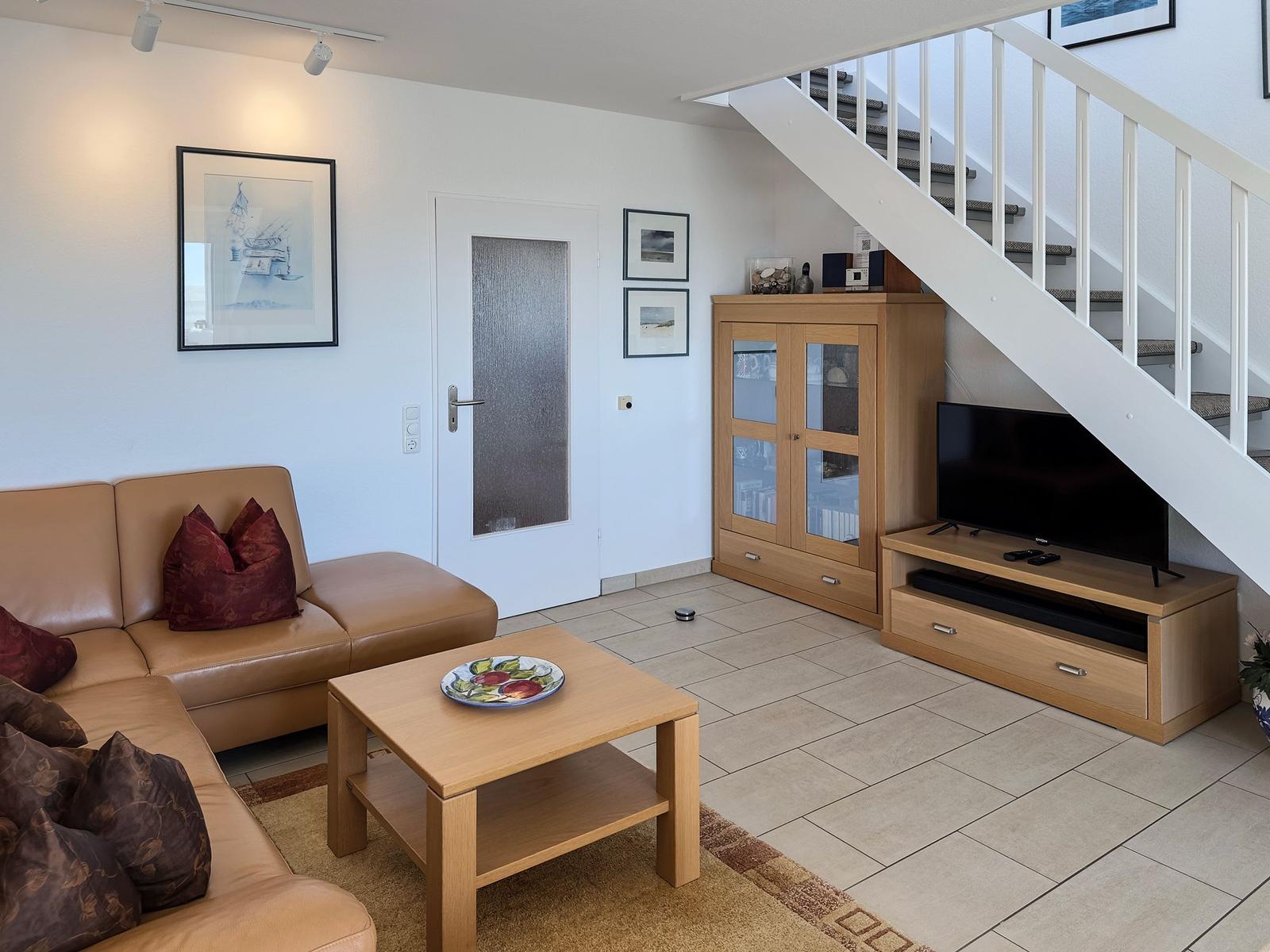 Wohnzimmer mit Sofa, Couchtisch und Fernseher unter Treppe.