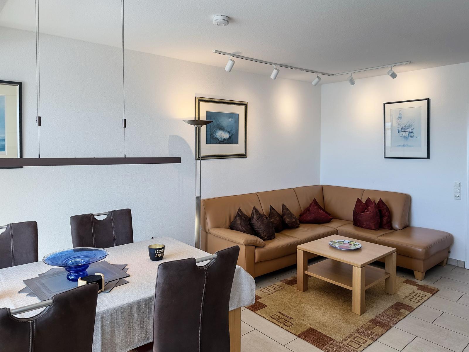 Wohn- und Essbereich mit Ledersofa, Tisch und Stühlen sowie Wandbildern.