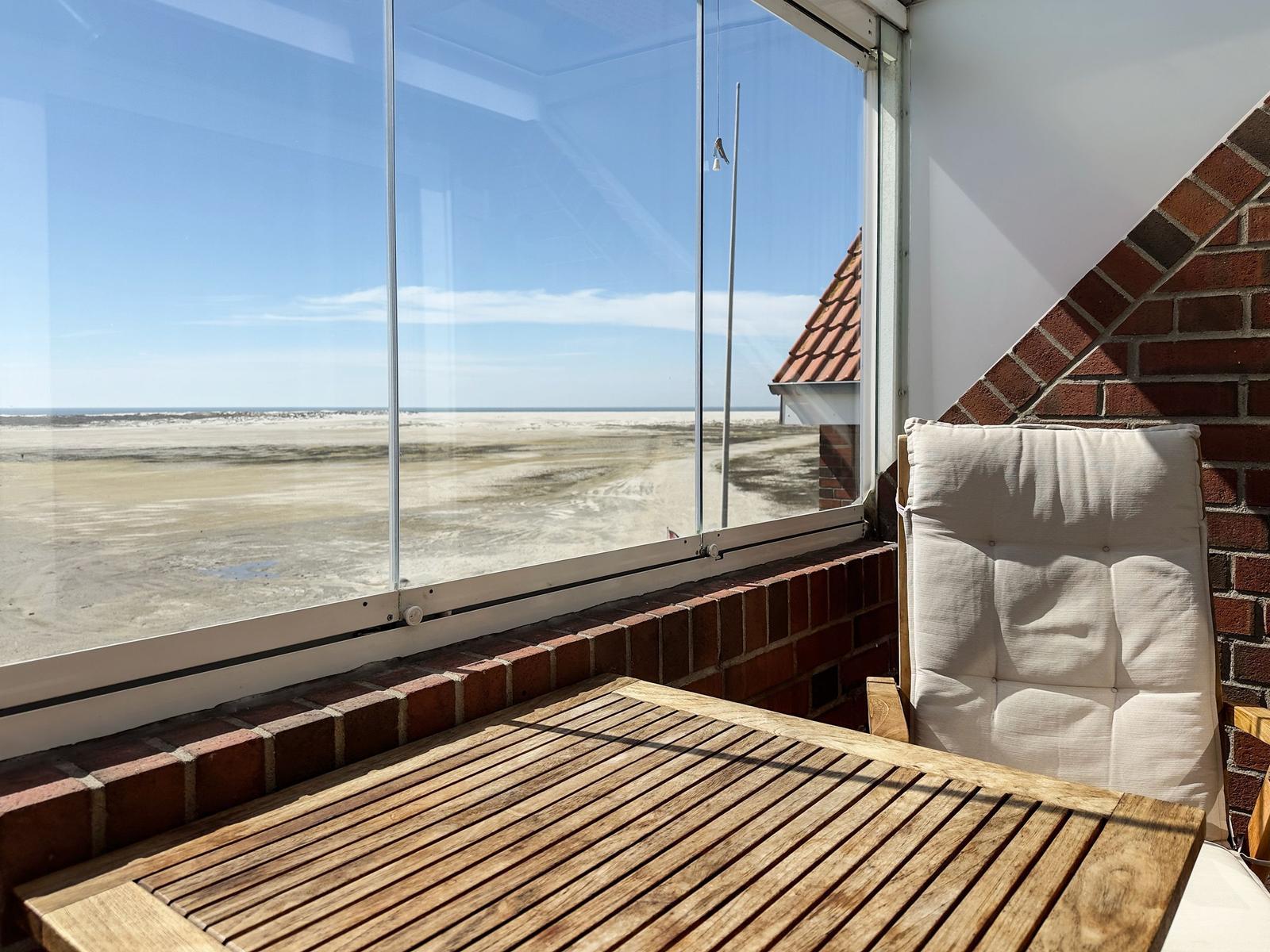 Terrasse mit Holztisch und Sitzkissen, Blick auf Strand und Meer.
