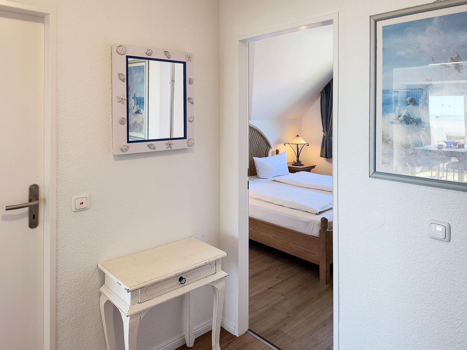 Schlafzimmer mit Bett und Nachttisch. Spiegel und Bild an der Wand. Tür links.
