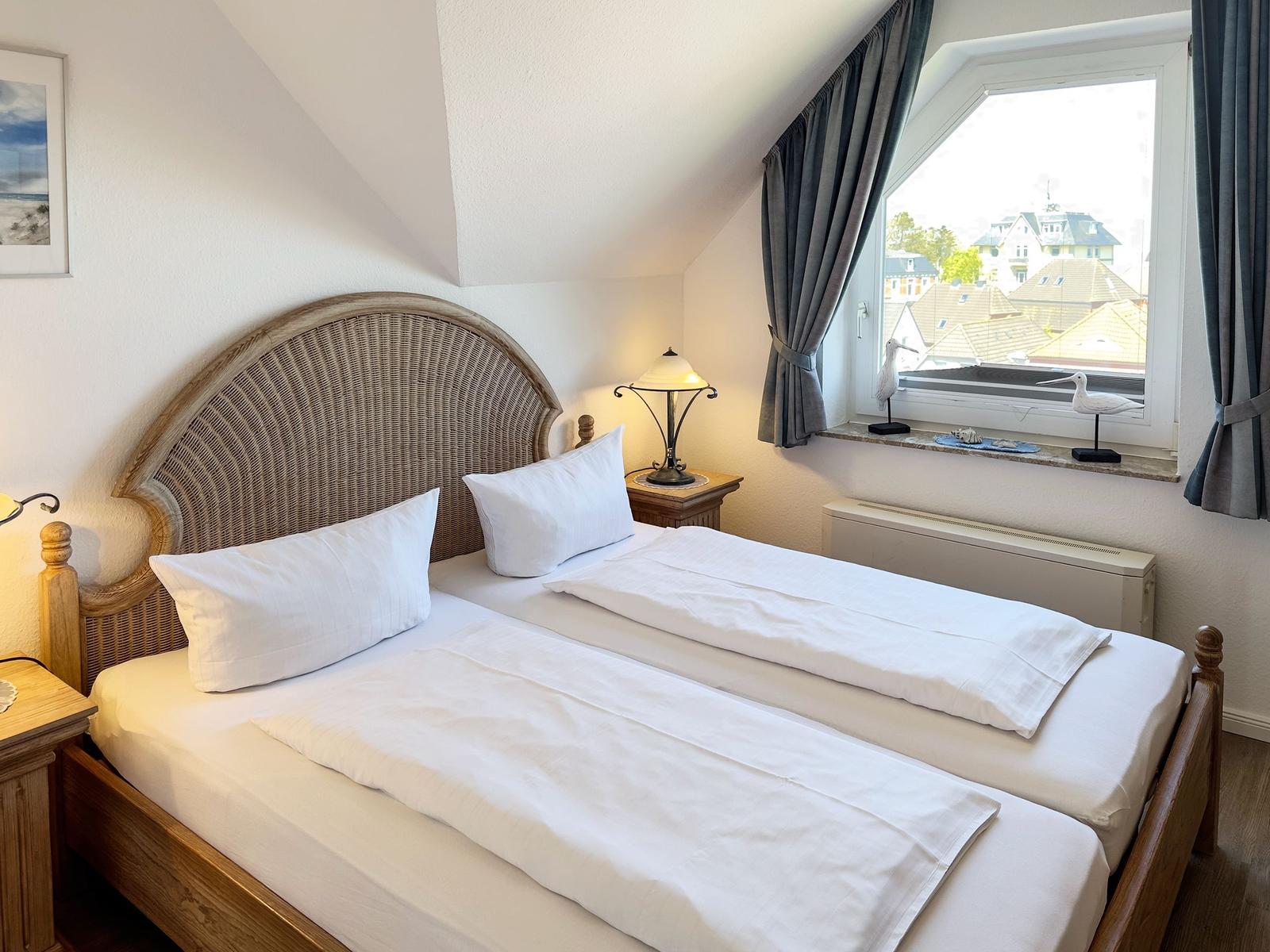 Zimmer mit Doppelbett, Fenster und Nachttisch. Blick auf Dächer.
