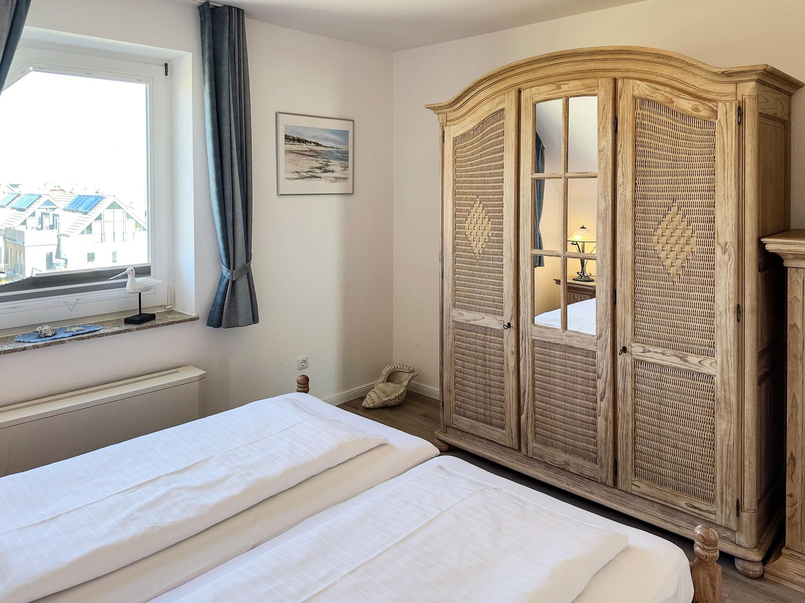Zimmer mit Doppelbett, Holzschrank und Fensterblick auf Dächer