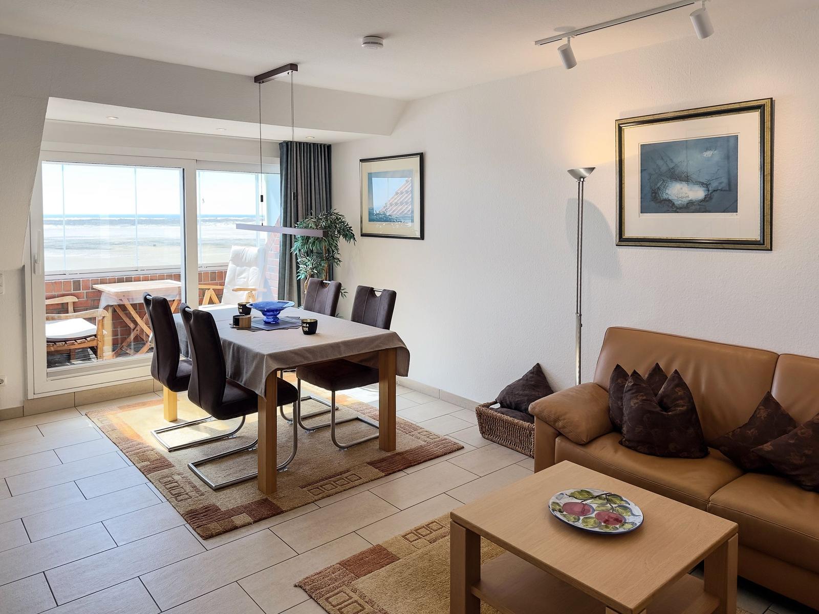 Wohn- und Essbereich mit Blick aufs Meer. Sofa, Tisch und Fenster sind sichtbar.