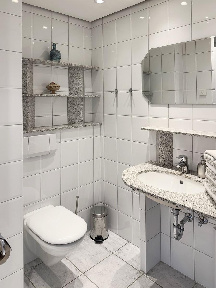 Badezimmer mit Toilette, Waschbecken und Regal mit Dekorationsgegenständen.