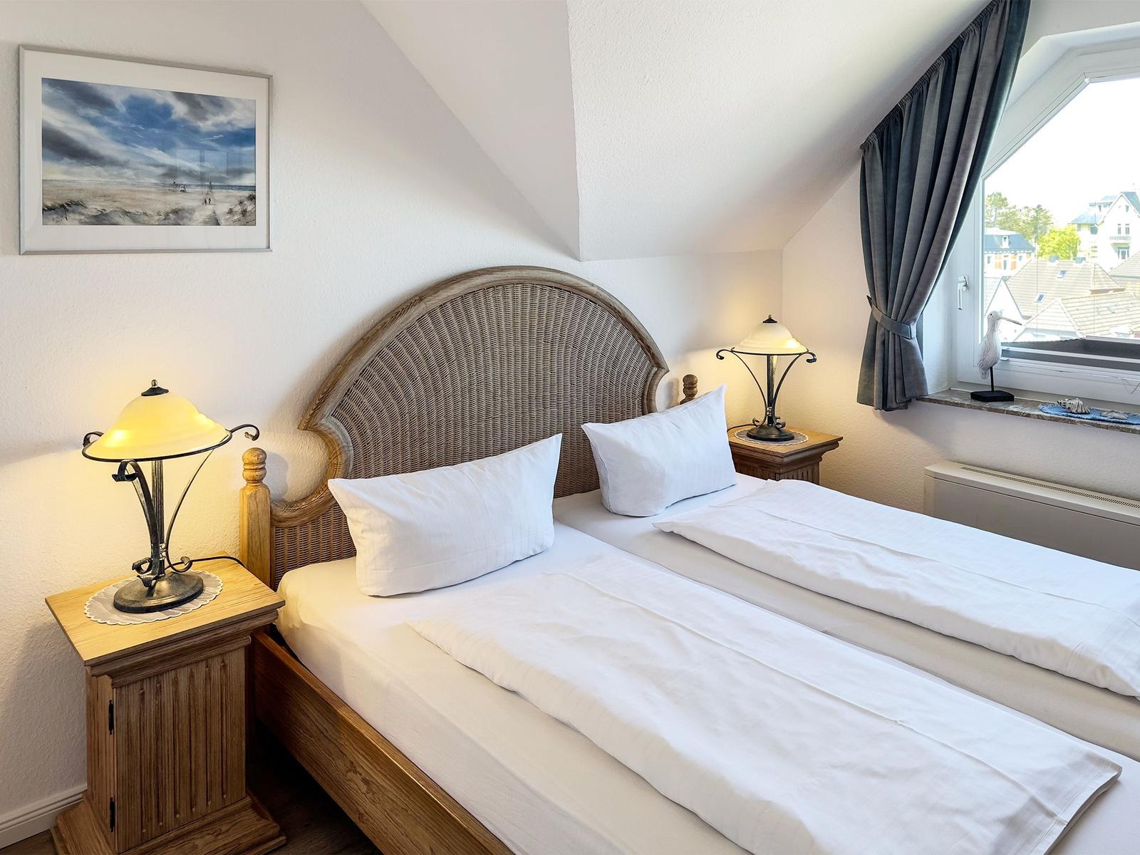 Schlafzimmer mit Doppelbett, zwei Nachttischen und Lampe. Fenster mit Blick auf Dächer.