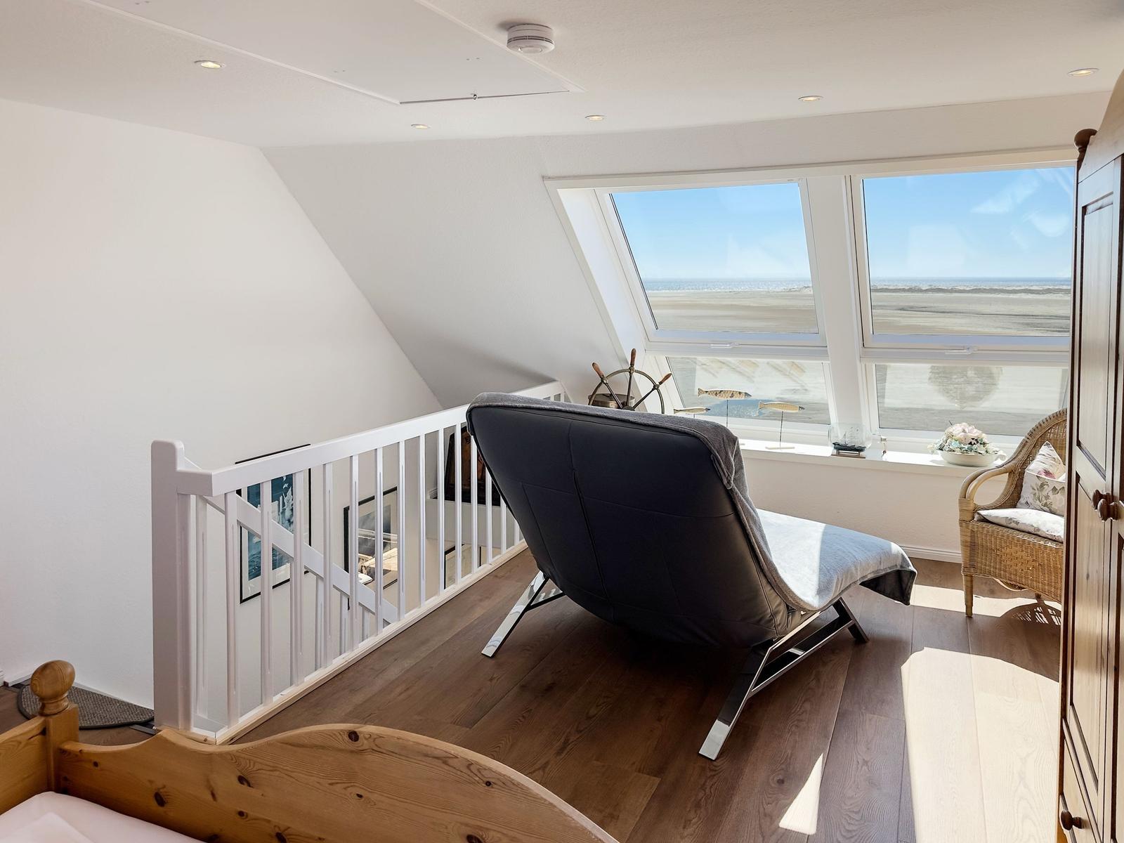 Dachgeschosszimmer mit Blick aufs Meer, schwarze Sessel, Holzboden und weißer Brüstung.