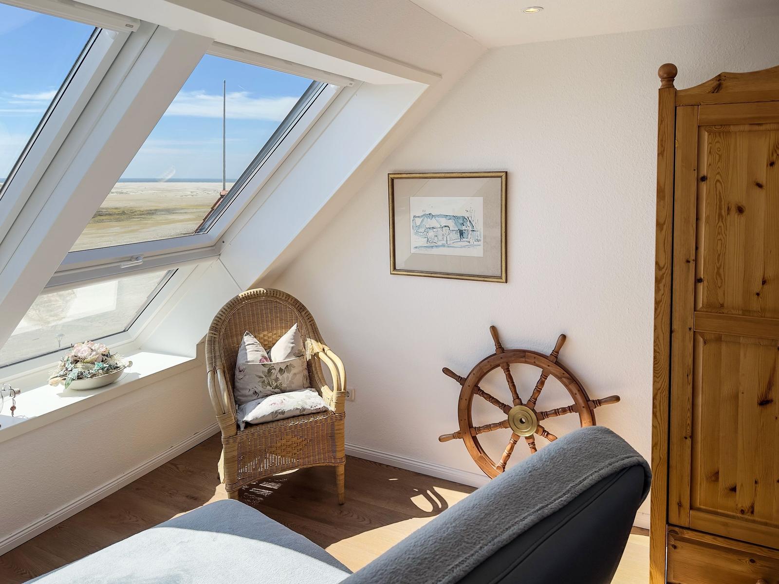 Ein Raum mit Dachfenster, Stuhl, Schiffsruder und Holzschrank.