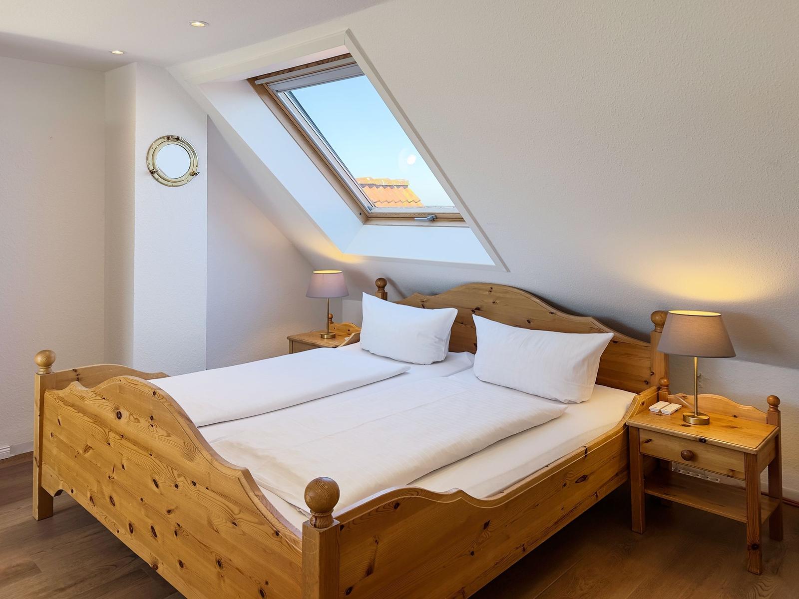 Ein Schlafzimmer mit Holzbett, zwei Nachttischen und einem Dachfenster.
