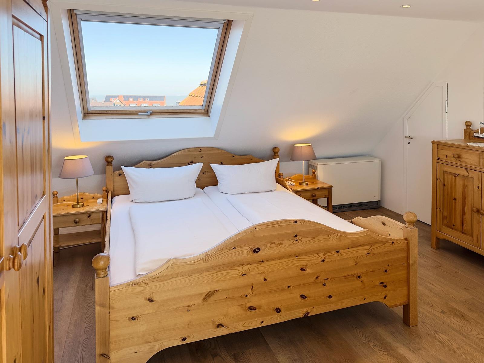 Schlafzimmer mit Holzbett, Fenster und Nachttischen.