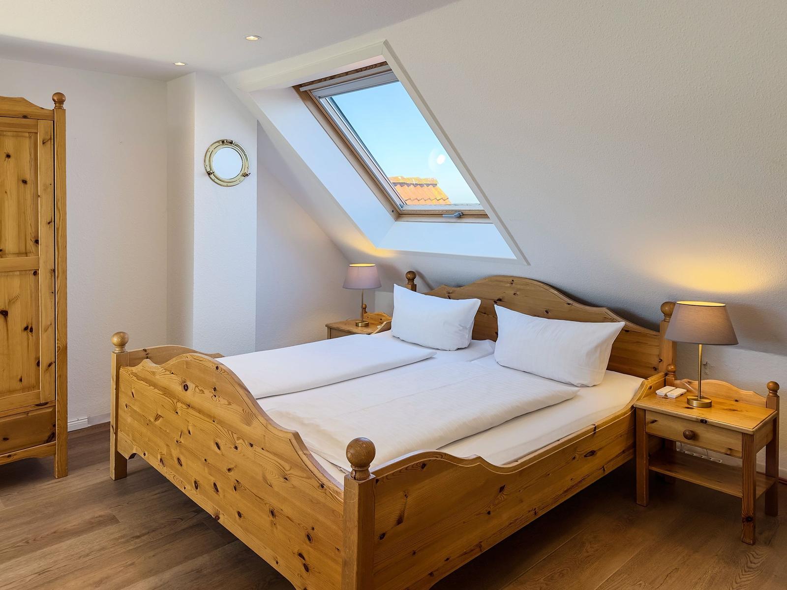 Schlafzimmer mit Holzbett, Nachttischen und Dachfenster. Holzschrank und runder Spiegel an der Wand.