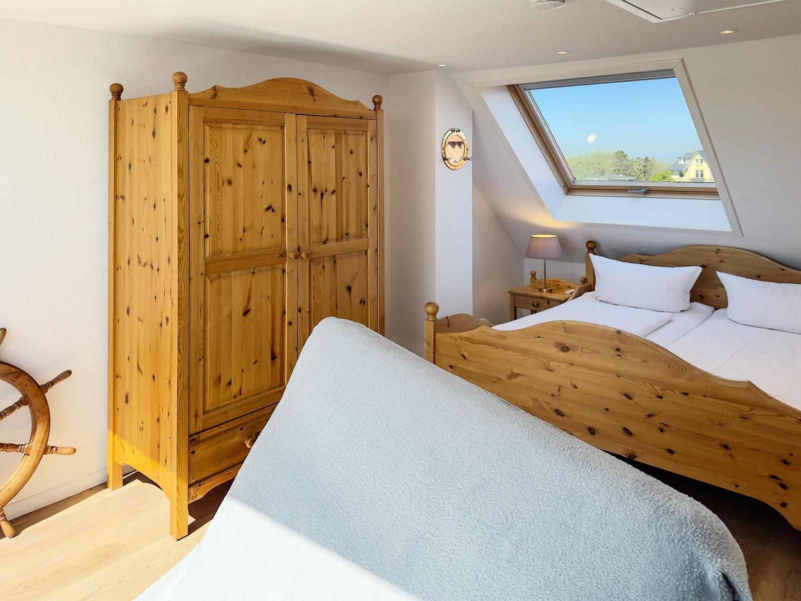 Schlafzimmer mit Holzbett, Kleiderschrank und Dachfenster. Blick auf die Umgebung.