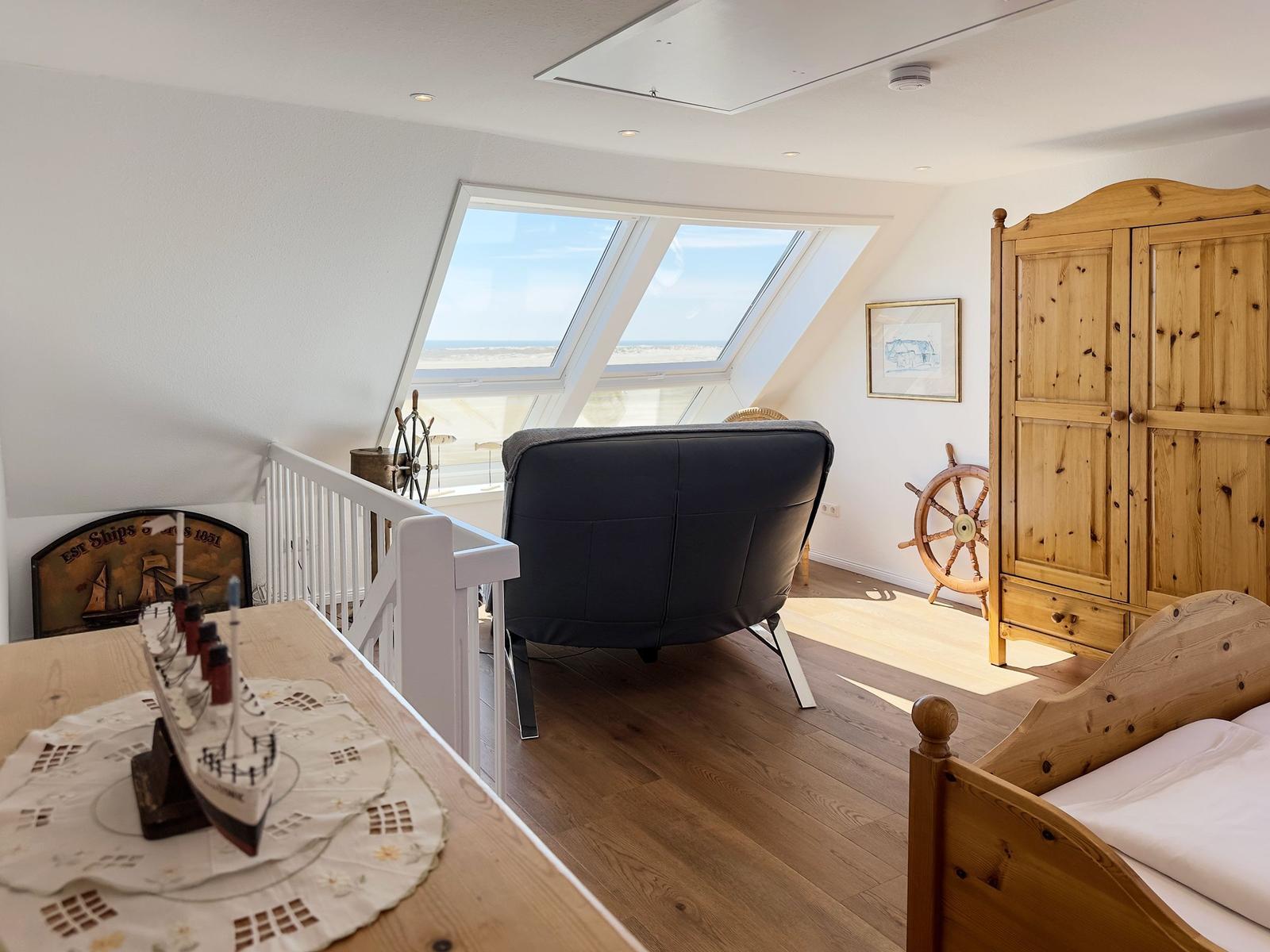 Schlafzimmer mit Blick aufs Meer, Holzbett, Kleiderschrank und Sitzgelegenheit.