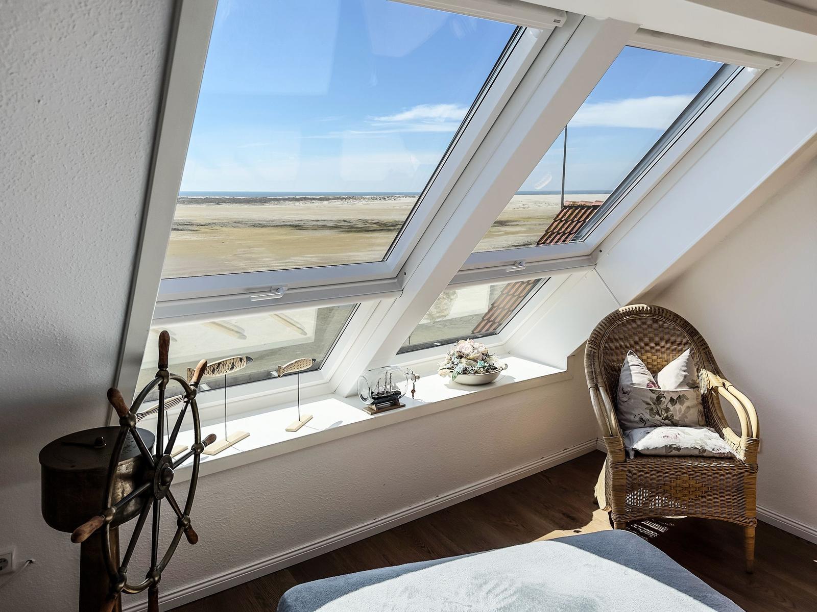 Dachzimmer mit Blick auf Strand und Meer, Wickerstuhl und Segelruder dekorieren den Raum.