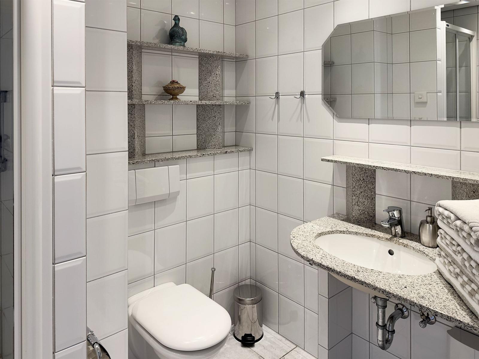 Badezimmer mit Toilette, Waschbecken und Spiegel. Weiße Fliesen und Marmorunterschrank.
