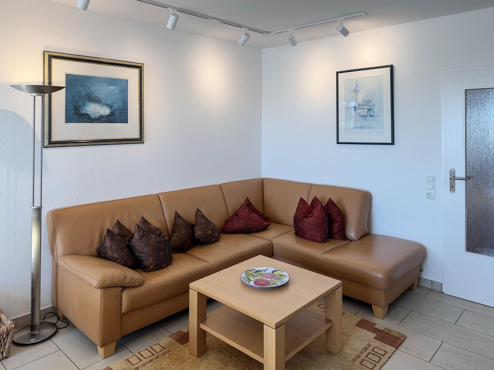 Ein Wohnzimmer mit braunem Sofa, Holztisch und Wandbildern.
