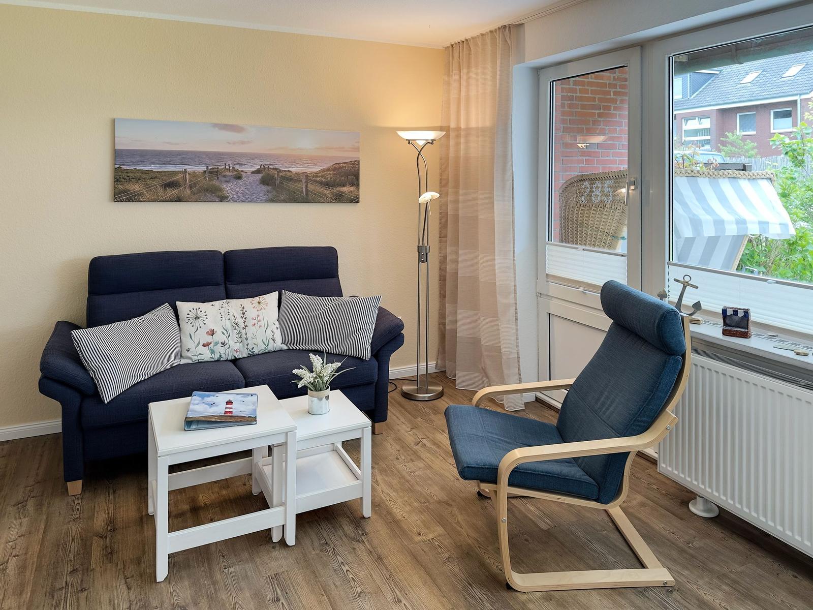 Ein Wohnzimmer mit Sofa, Sessel, Tisch und Fensterblick.