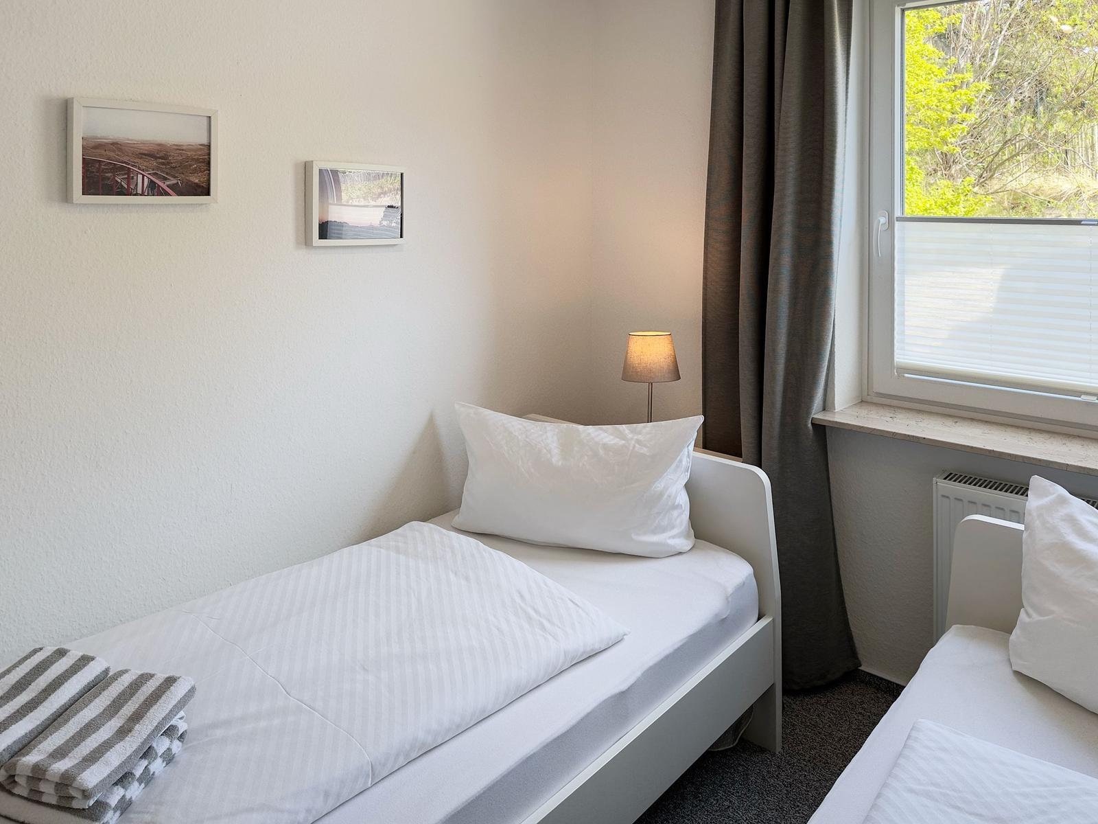 Zimmer mit zwei Betten, Fenster mit Blick auf Bäume und Lampen an der Wand.