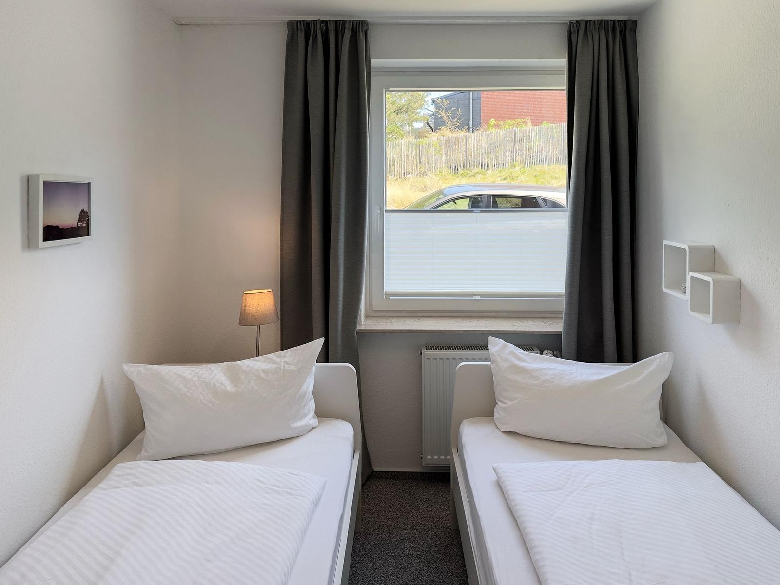 Zwei Einzelbetten, Fenster mit Jalousie und Vorhang, Wandlampe und Bild.